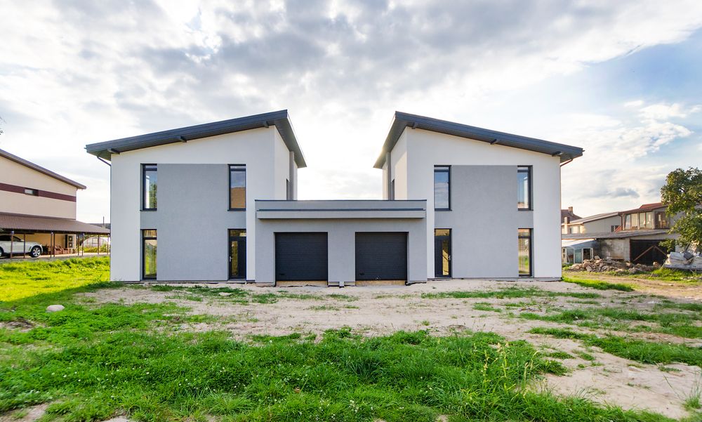 Two new white two-storey houses with dark garage doors on a fresh lawn